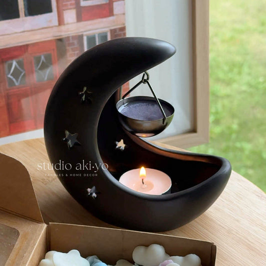 Black moon-shaped candle holder with a lit candle inside, placed on a wooden surface.