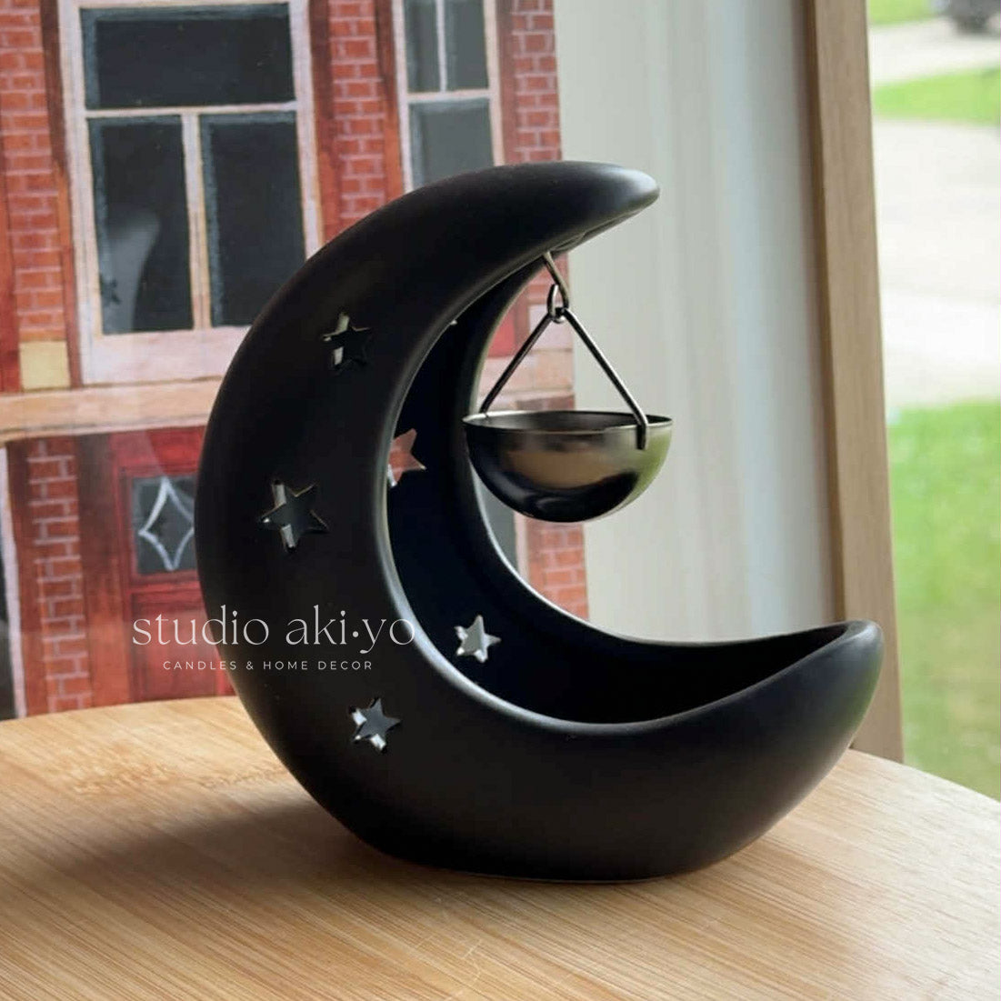 Black moon-shaped candle holder with stars on a wooden surface, brand 'studio aki-yo' visible.