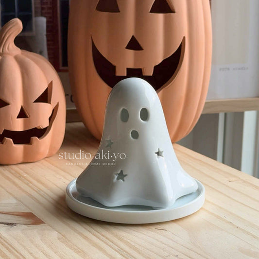 White ceramic ghost decoration with star patterns on a wooden surface, with pumpkins in the background.