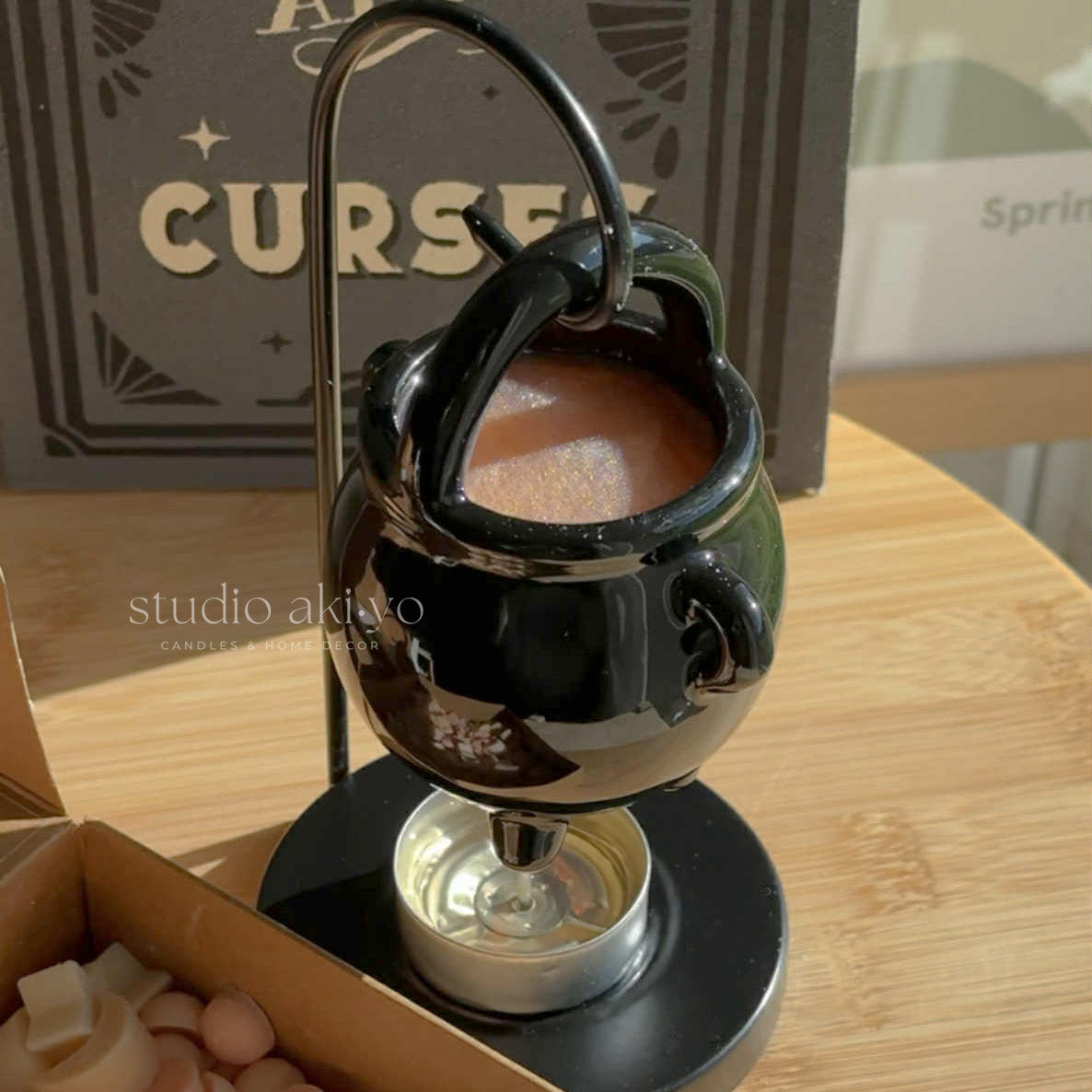 Black decorative item resembling a teapot on a wooden surface with 'studio akiko' branding.