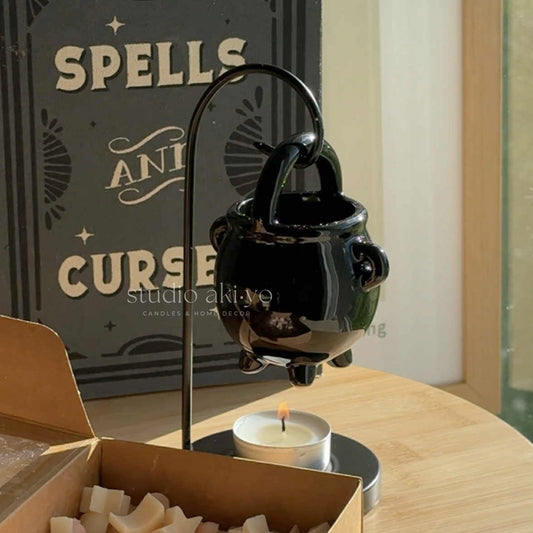 Decorative black teapot with a candle on a wooden surface, with 'Spells and Curses' book in the background.