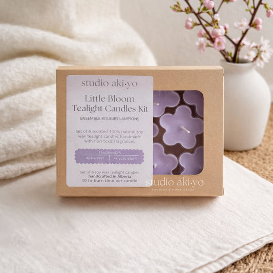 Studio Akiyo Little Bloom Tealight Candles Kit packaging on a soft surface with a vase of flowers in the background.