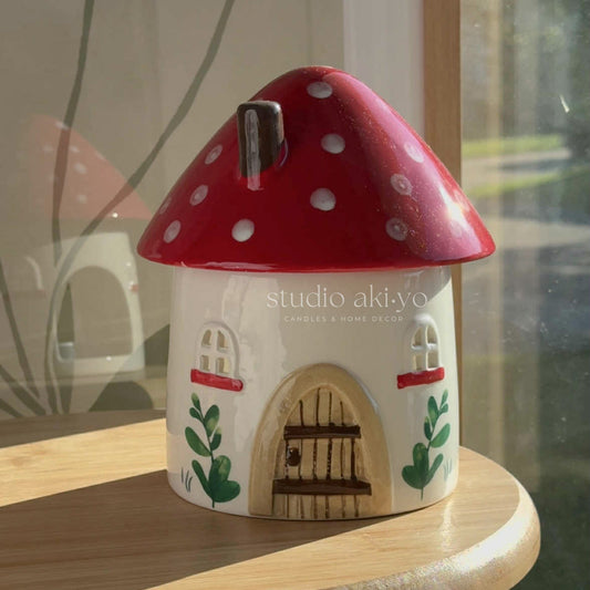 Decorative mushroom-shaped house candle on a wooden surface with 'studio akiyo' branding.