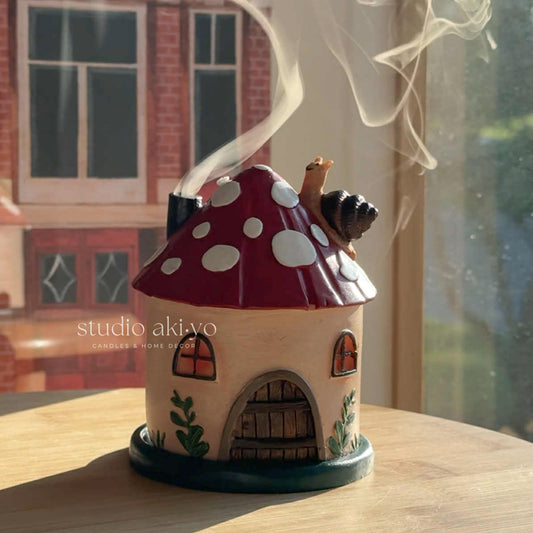 Ceramic mushroom-shaped house with a chimney and smoke, on a wooden surface.