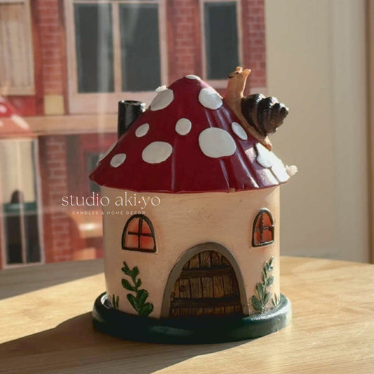 Fairy house with red mushroom roof on a wooden surface, brand 'studio akiyo' visible