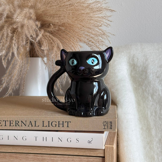 Enjoy a spellbinding sip from this cat-shaped ceramic mug, featuring striking blue eyes and an adorable curled tail for a handle. A unique gift for lovers of gothic and witchy aesthetics.