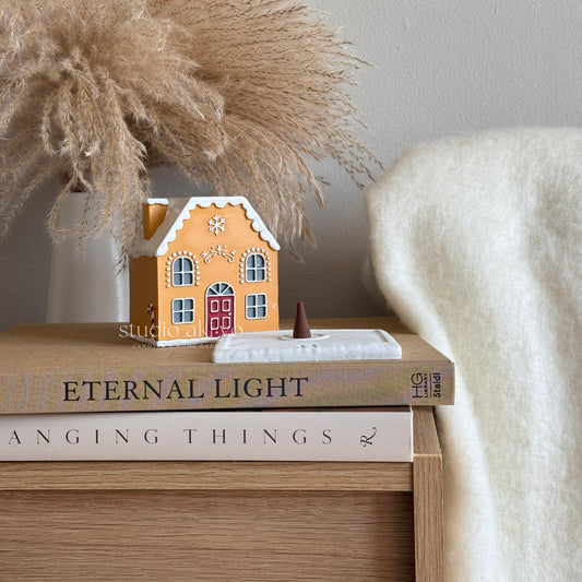 Decorative gingerbread house on books with pampas grass and a vase in the background