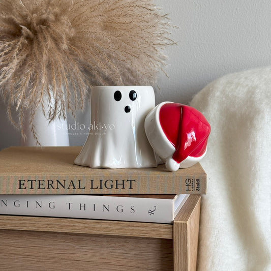 White ghost figurine with a red hat on top of books with a neutral background