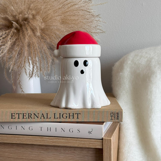 White ghost-shaped wax melt burner with a red Santa hat on top of books, with 'studio akiyo' branding.