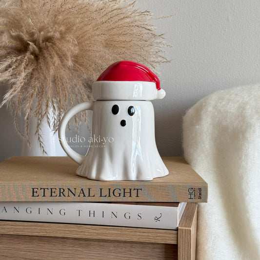 Ghost-shaped mug with a Santa hat on top of books, with 'studio aki-yo' branding.