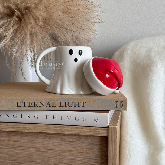 White ghost mug with a red interior on top of books with a decorative background
