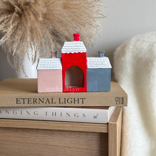 Three small houses in red, pink, and blue on top of books with decorative elements in the background.