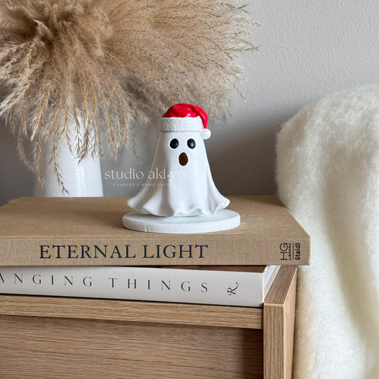 Small ghost figurine with a Santa hat on top of books, with 'studio akiko' branding in the background.
