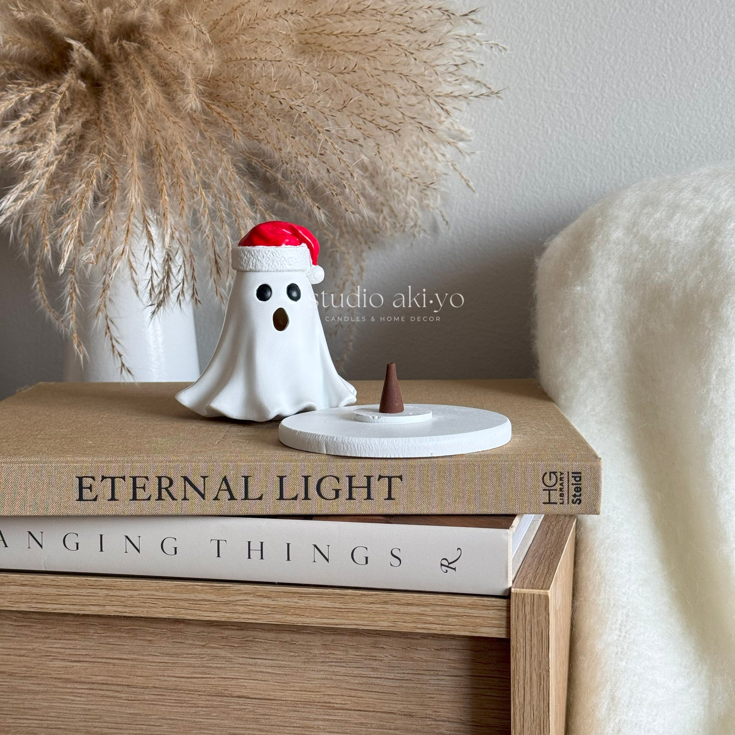 Small ghost figurine with a Santa hat on top of books, with 'studio akiyo' branding.
