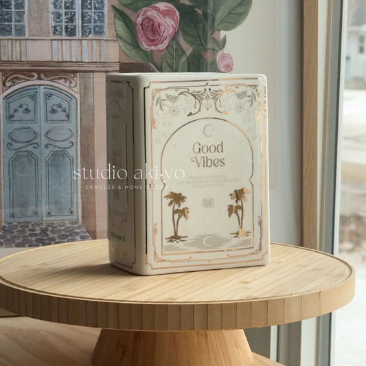 Candle box labeled 'Good Vibes' on a wooden table with decorative elements in the background