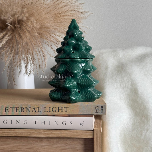 Green ceramic Christmas tree-shaped lantern on books with a neutral background