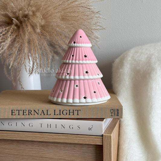 Pink Christmas tree wax melt burner on a stack of books with a neutral background