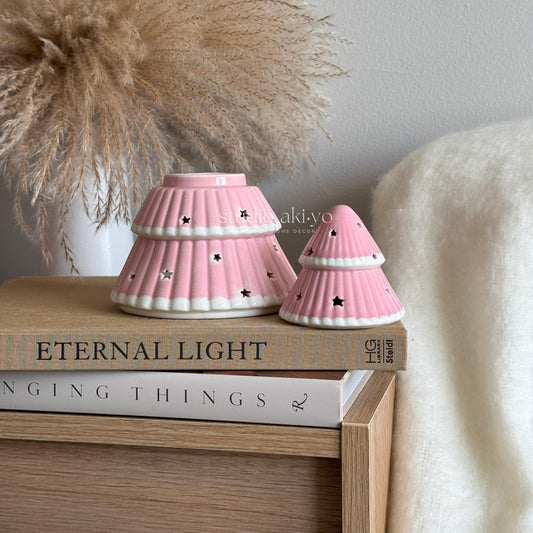 Two pink ceramic lamps on a stack of books with decorative elements in the background.