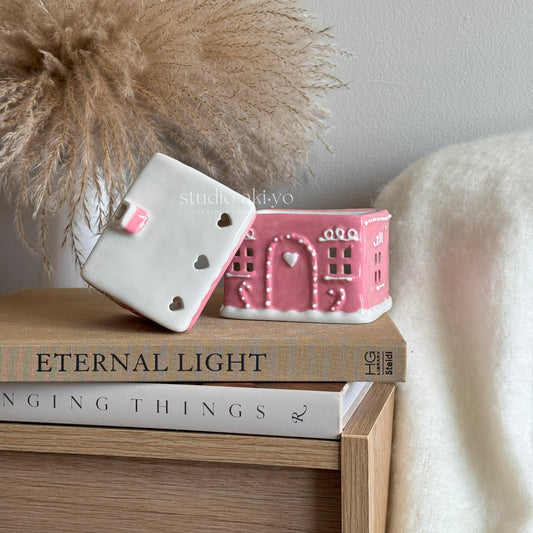 Pink ceramic gingerbread house wax melt burner on top of books with a decorative background