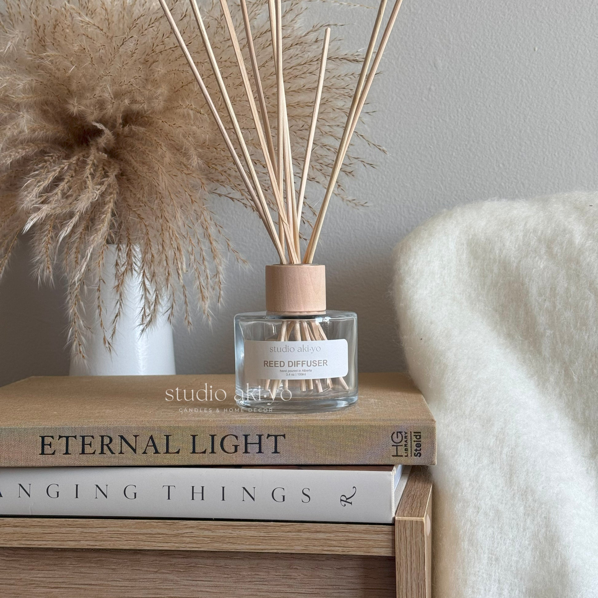 Clear glass reed diffuser with wooden cap and natural rattan reeds, styled on a neutral background. Minimalist home fragrance decor winterberry scented
