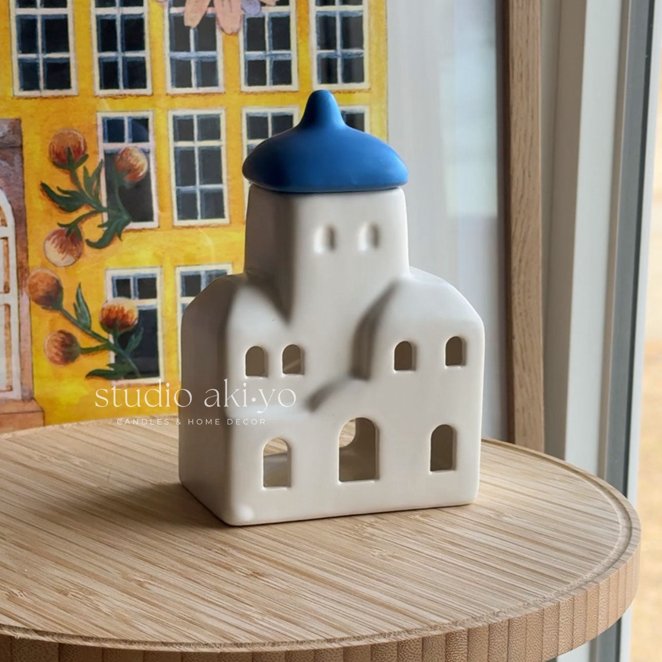 Ceramic house-shaped object with a blue roof on a wooden surface, with 'studio akiyo' branding.