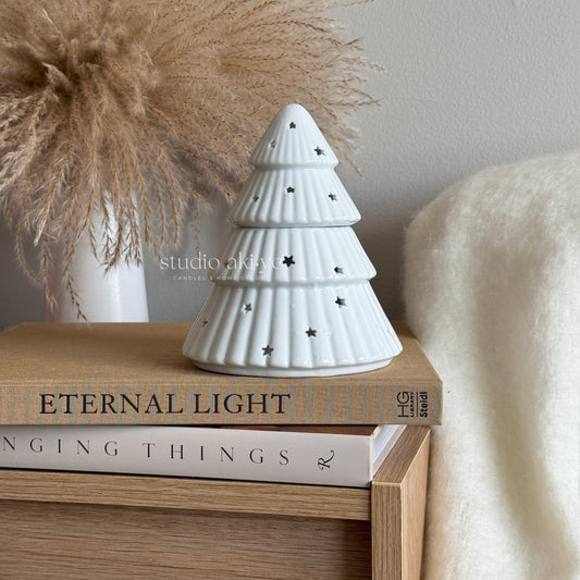 White ceramic Christmas tree wax oil burner on books with a neutral background
