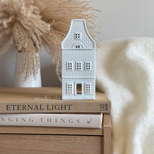 White scandi nordic ceramic house-shaped burner  on a stack of books with decorative elements in the background