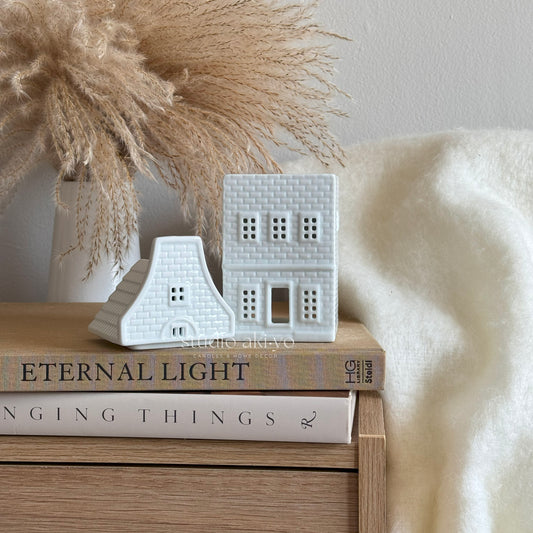Decorative white ceramic houses on books with a pampas grass arrangement in the background.