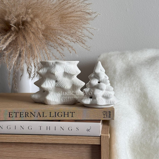 White winter fir tree ceramic Christmas burner on a stack of books with decorative elements in the background.
