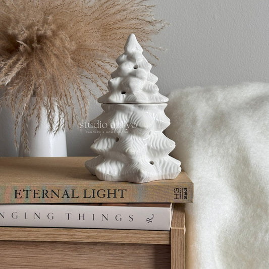 White ceramic Christmas tree ornament on a stack of books with a neutral background