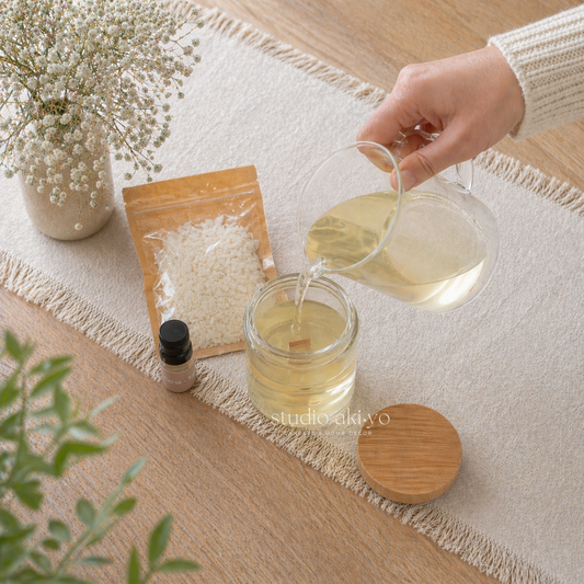 Hand pouring liquid into a glass jar on a wooden surface with plants and a white cloth.