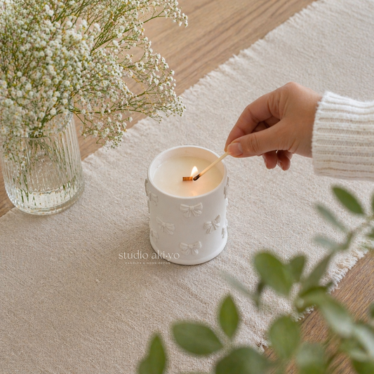 Hand lighting a white candle with floral design on a textured surface, next to a vase of flowers.
