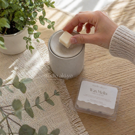 Person taking Studio Akiyo's soy wax melt from a container on a wooden surface with plants around.