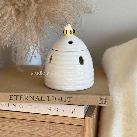 White ceramic beehive wax melt burner with honeycomb cutouts and bee on lid