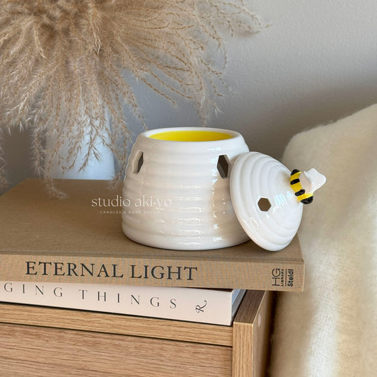 White ceramic beehive wax melt burner with honeycomb cutouts and bee on removable lid