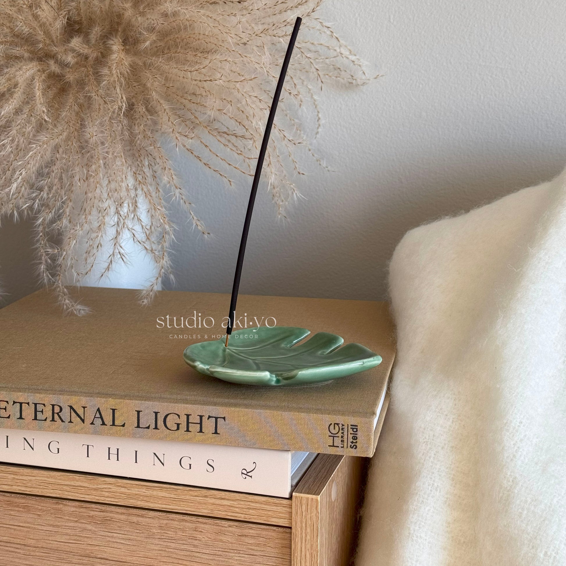 Leaf incense holder with stick upright and ashes resting on surface