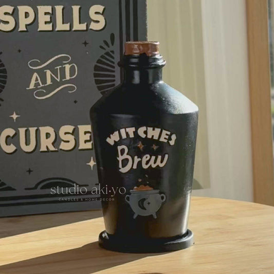 Black bottle labeled 'Witches Brew' on a wooden surface with a decorative sign in the background.