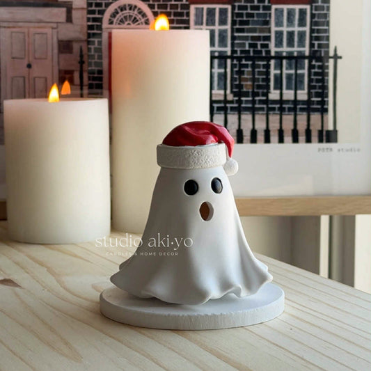 Ghost figurine with a Santa hat in front of lit candles on a wooden surface.