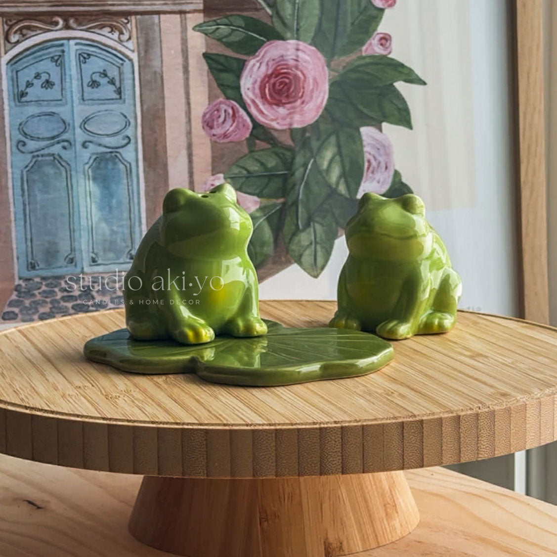 Two green ceramic frogs on a wooden surface with a decorative background