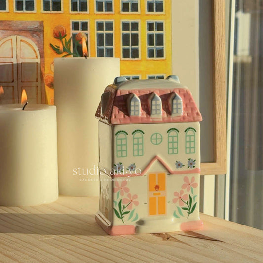 Decorative house-shaped candle with floral designs on a wooden surface.