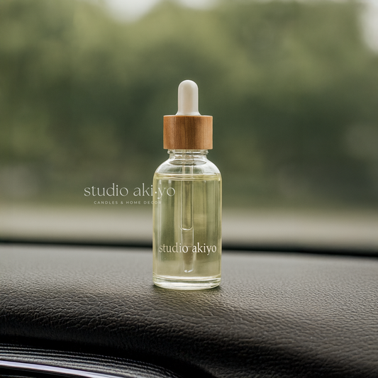 Hanging car diffuser refill in a clear glass dropper bottle with wooden cap on a car dashboard, featuring 'studio akiyo' branding.