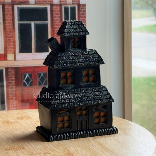 Black salem witches house-shaped candle holder on a wooden surface with a blurred background