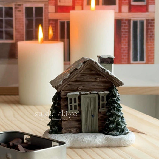 Decorative house-shaped candle holder with candles on a wooden surface.