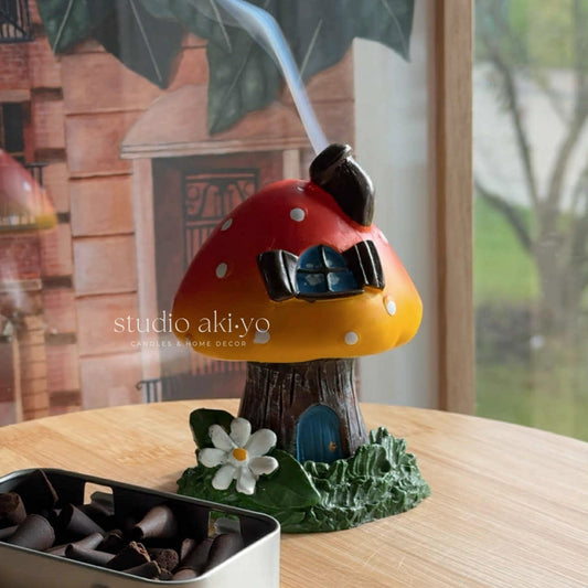 Decorative mushroom-shaped toadstool incense cone burner with a small door and flower on a wooden surface. Enjoy the smoke going through the little chimney for those whimsical cottagecore fairy vibes.
