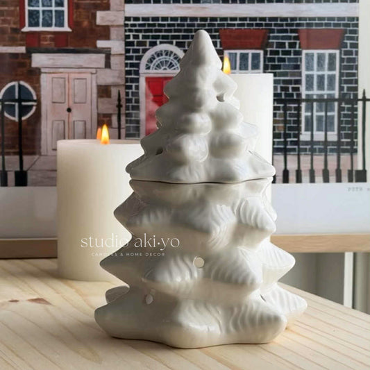 White ceramic tree-shaped diffuser with a candle in front of a decorative fireplace.