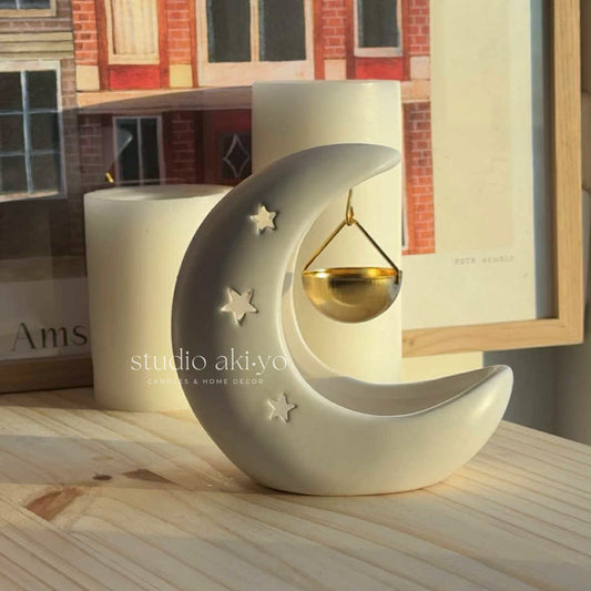 Decorative moon-shaped candle holder with a lit candle on a wooden surface, featuring the brand 'studio akiyo'.