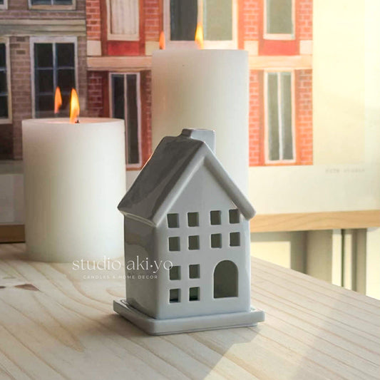 White house-shaped incense cone holder with a lit candle on a wooden surface.