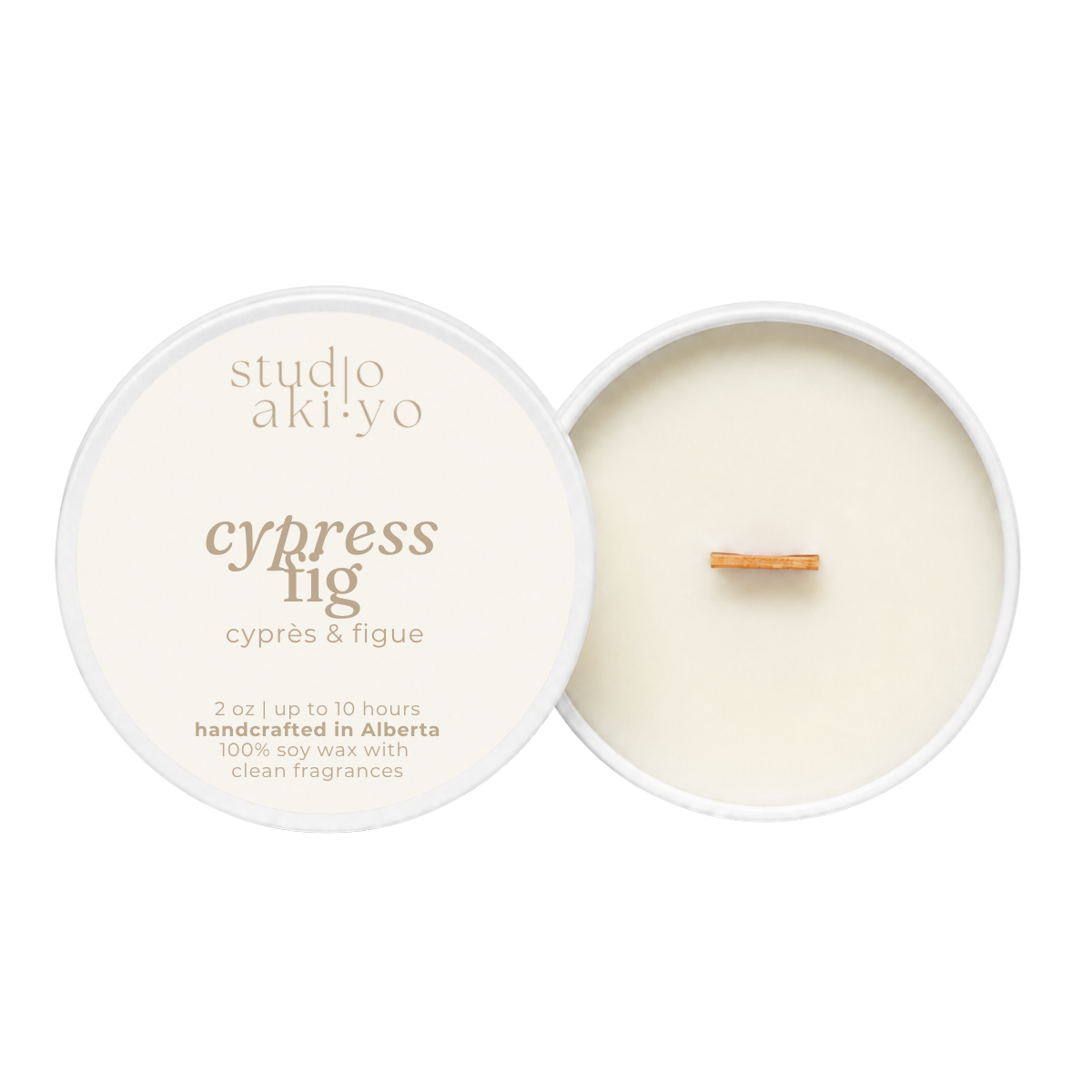 An open soy wax candle by studio akiyo, showing the cream-colored wax and wick inside a white round tin next to its lid, which is printed with the scent name 'cypress fig' and notes 'handcrafted in Alberta'.
