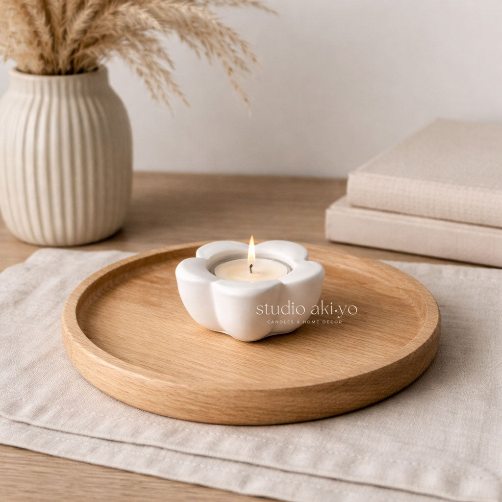 Candle in a white holder on a wooden tray with a vase of dried grasses in the background.
