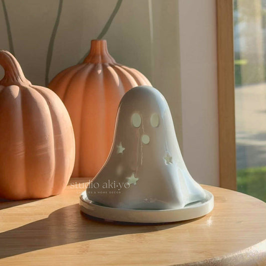 Ghost-shaped lantern with star cutouts on a wooden surface with pumpkins in the background